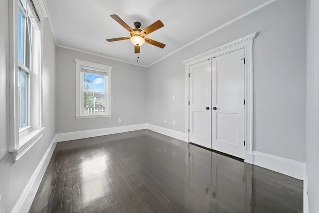 an empty room with wooden floor chandelier fan and windows