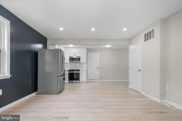 a view of an empty room with kitchen and window