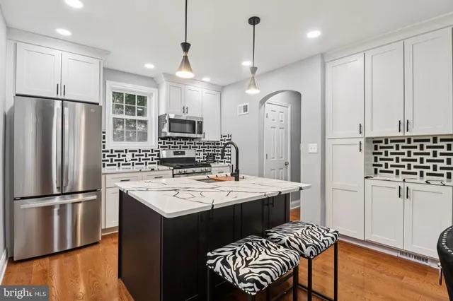 a kitchen with stainless steel appliances granite countertop a refrigerator a sink dishwasher a stove and white cabinets with wooden floor