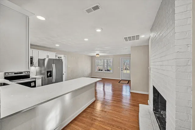 a large white kitchen with stainless steel appliances refrigerator a oven and a fireplace with wooden floor