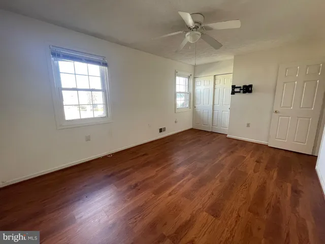an empty room with wooden floor chandelier fan and windows