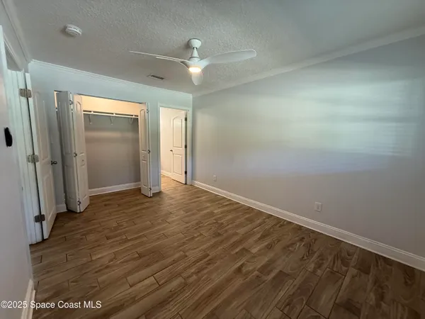 an empty room with wooden floor and a ceiling fan