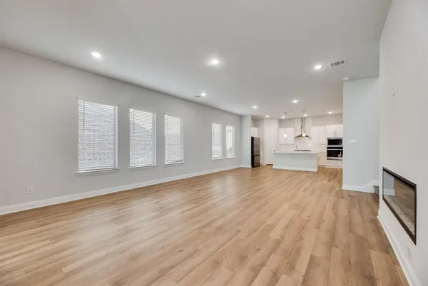 a view of an empty room with wooden floor and a kitchen