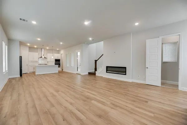a view of an empty room with wooden floor and a kitchen