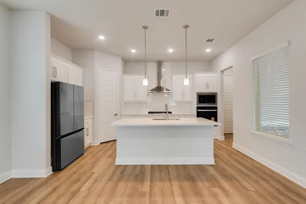 a large kitchen with stainless steel appliances a large counter top and a refrigerator