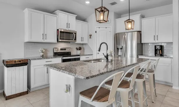a kitchen with stainless steel appliances granite countertop a sink a microwave a refrigerator and white cabinets