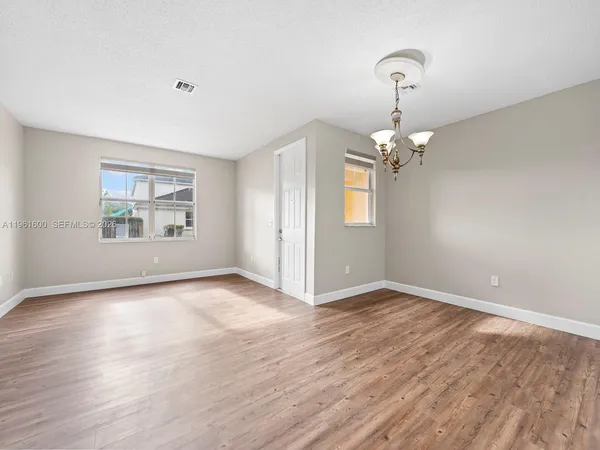 an empty room with wooden floor chandelier and windows