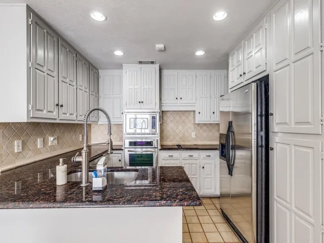 a kitchen with kitchen island granite countertop a refrigerator a stove and white cabinets with wooden floor