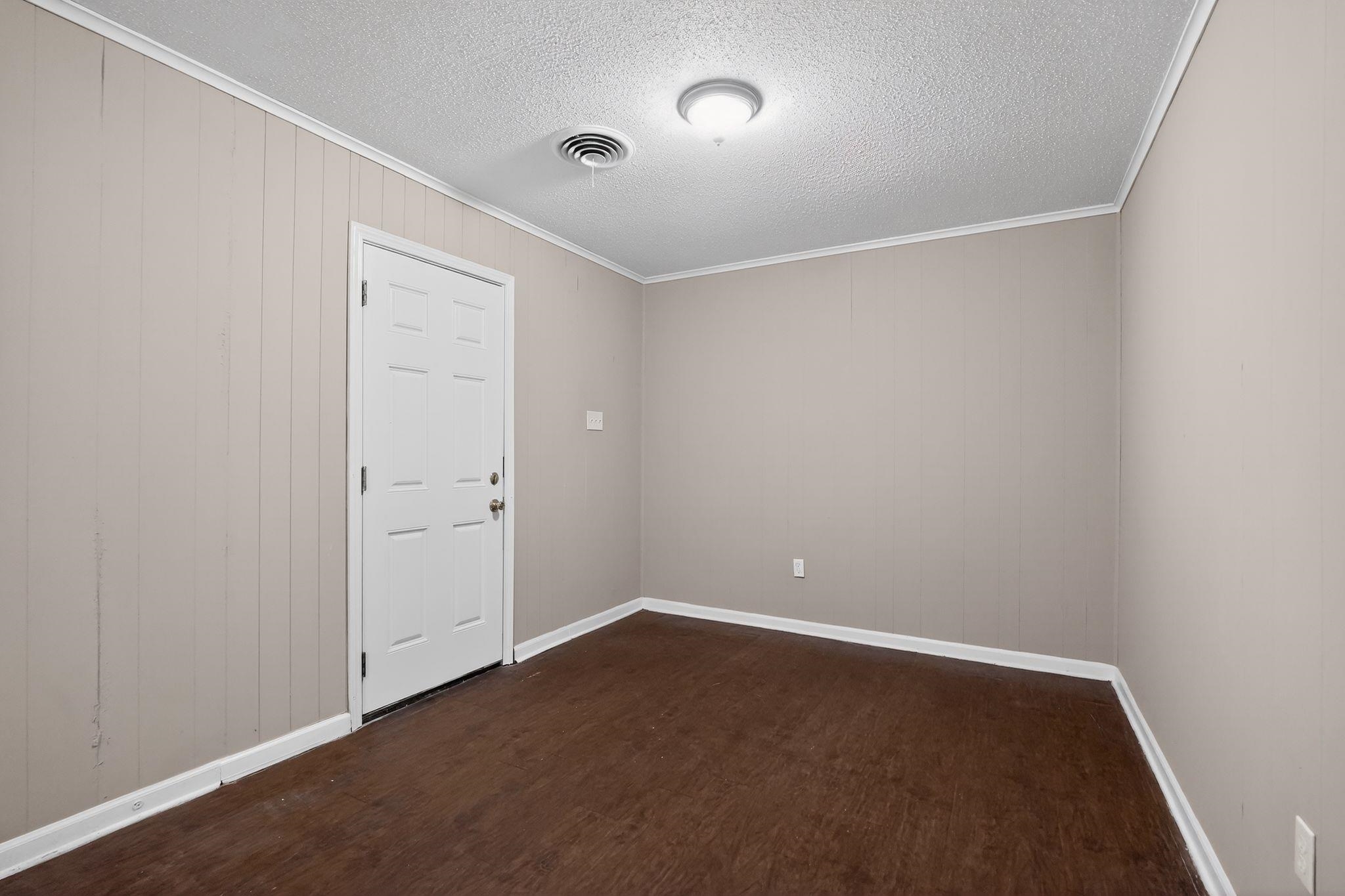 4587 Appleville Street Memphis, TN 38109 - Photo 13 of 34 Spare room featuring dark wood-type flooring, ornamental molding, a textured ceiling, and wooden walls