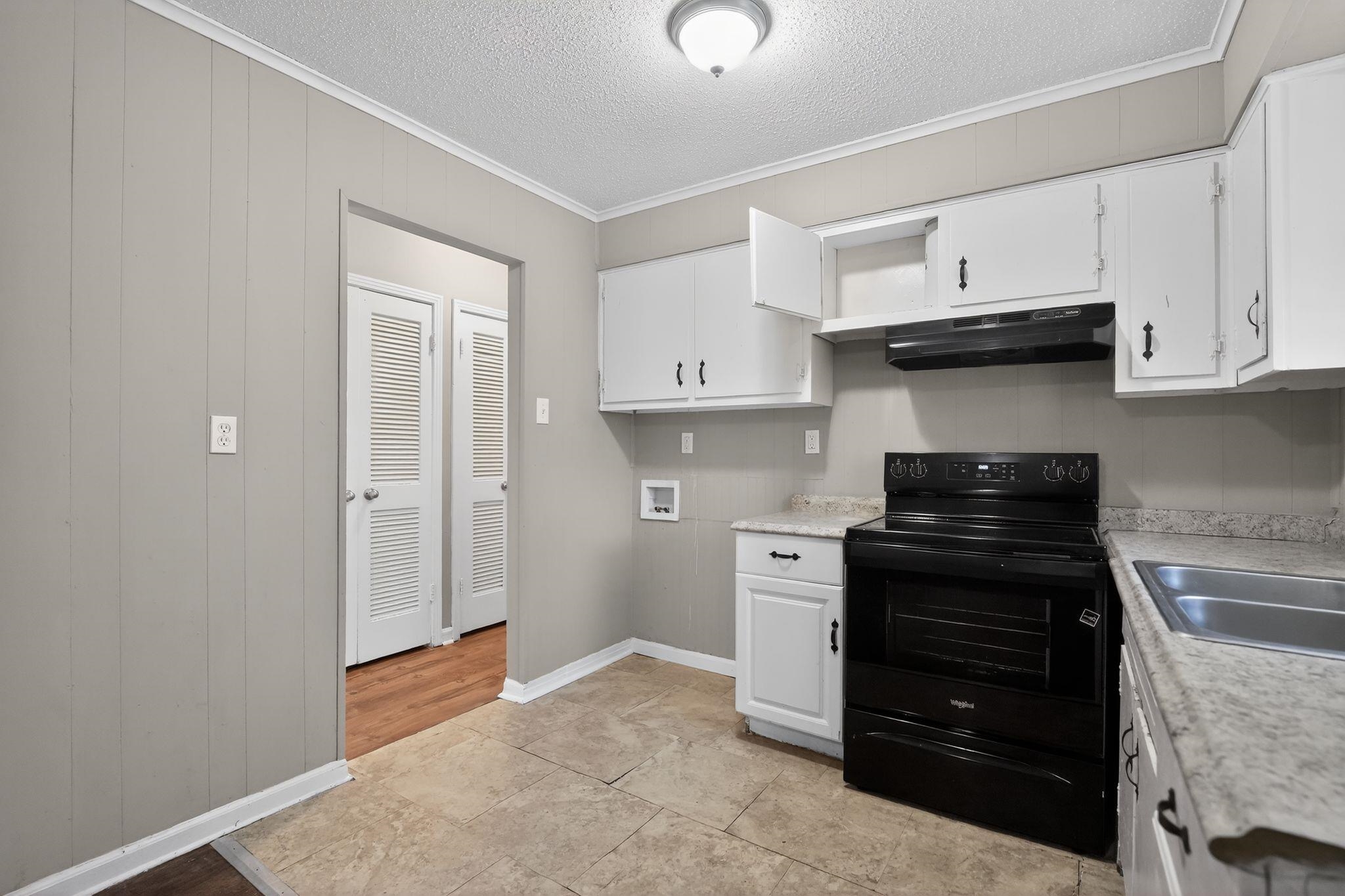 4587 Appleville Street Memphis, TN 38109 - Photo 16 of 34 Kitchen with electric range, white cabinets, ornamental molding, light countertops, and wood walls