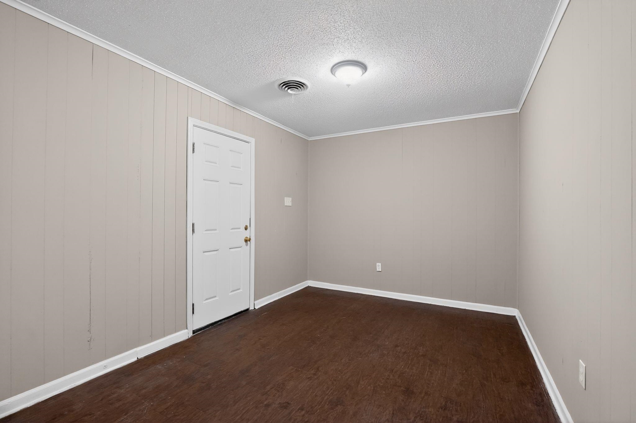 4587 Appleville Street Memphis, TN 38109 - Photo 6 of 34 Empty room featuring dark wood-style floors, ornamental molding, a textured ceiling, and wooden walls