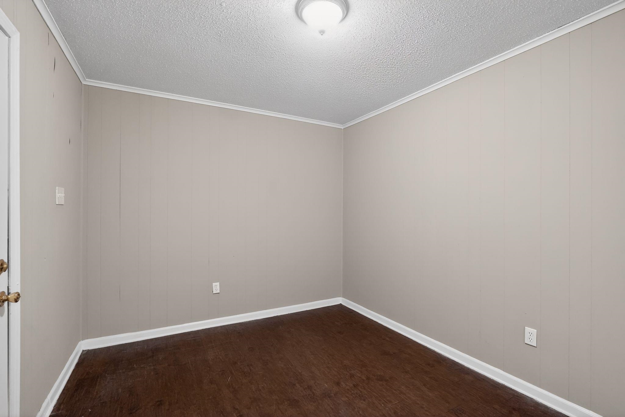 4587 Appleville Street Memphis, TN 38109 - Photo 9 of 34 Unfurnished room featuring dark wood-style floors, a textured ceiling, wooden walls, and ornamental molding