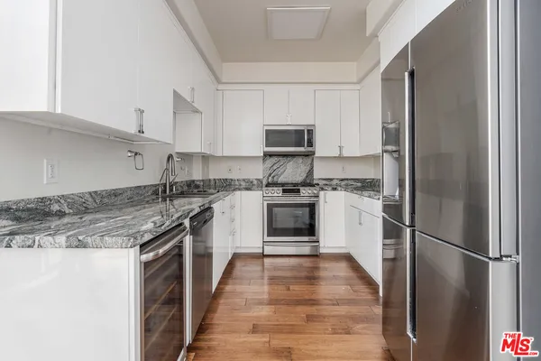 a kitchen with stainless steel appliances granite countertop a refrigerator a stove a sink and white cabinets