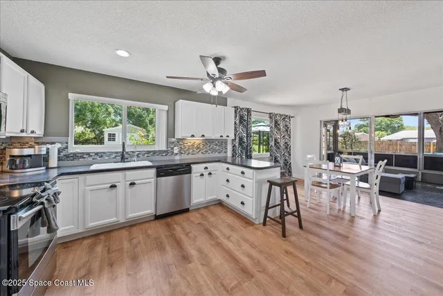 a large white kitchen with granite countertop a stove a sink a dining table and chairs with wooden floor