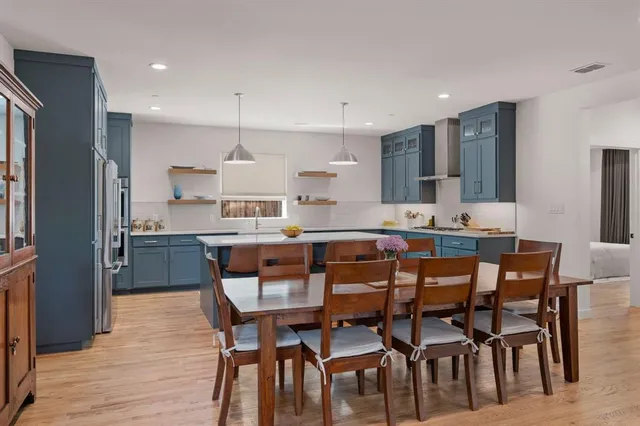 a kitchen with stainless steel appliances kitchen island granite countertop a dining table chairs and a refrigerator