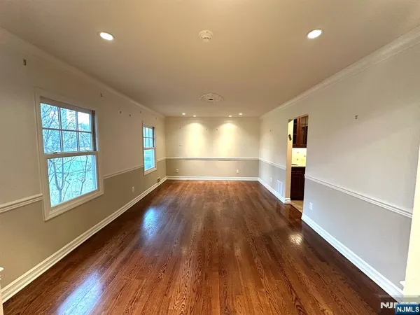 an empty room with wooden floor kitchen view and windows