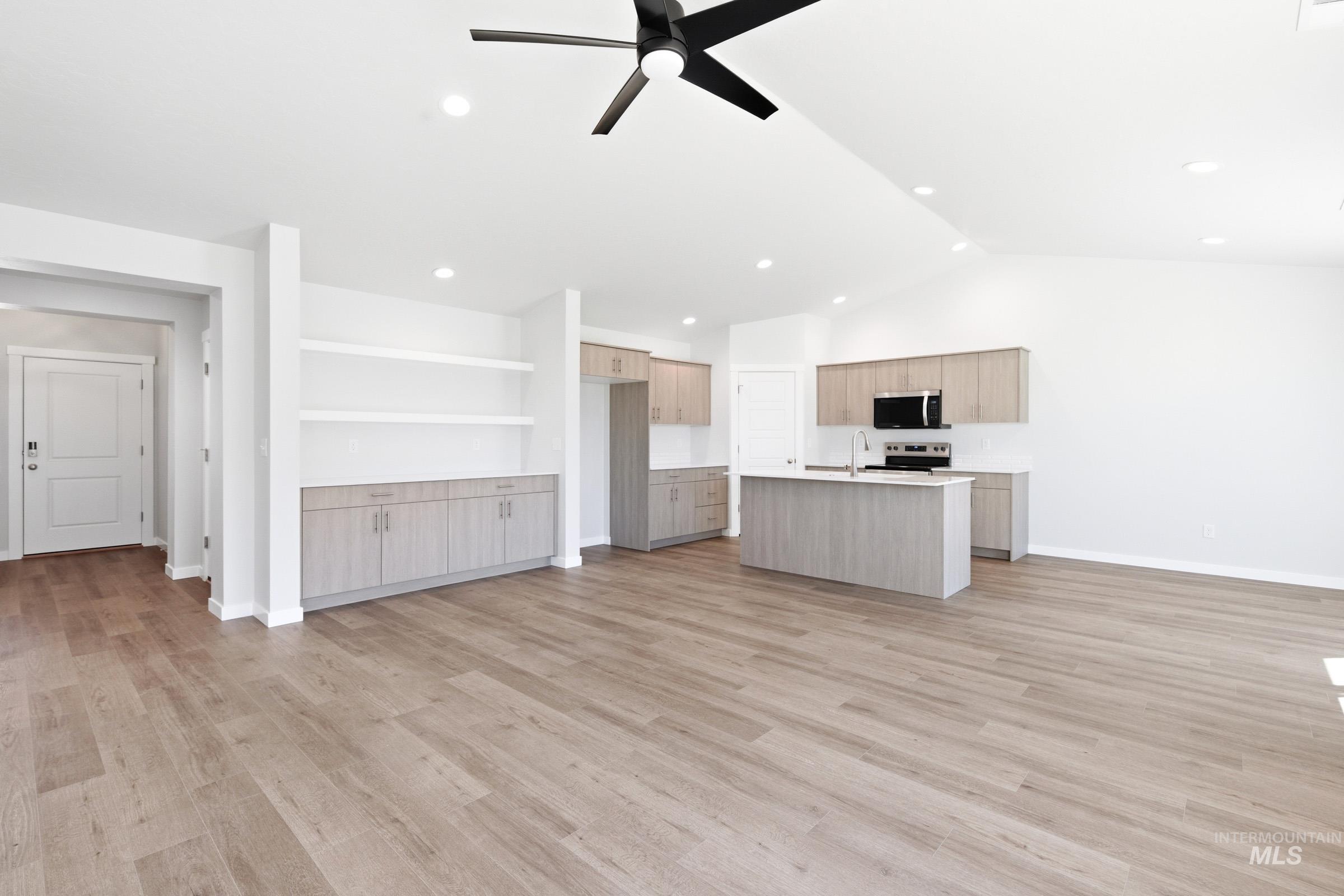 12877 Decatur Street Nampa, ID 83651 - Photo 14 of 22 Open-concept living area featuring wood-finish flooring, a contemporary kitchen with light-toned cabinetry and an island, a built-in storage unit with open shelving, recessed lighting, and a vaulted ceiling with a modern ceiling fan