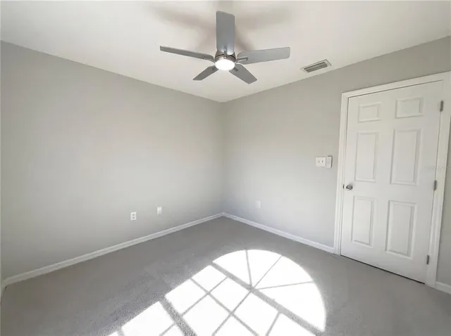an empty room with a chandelier fan and windows