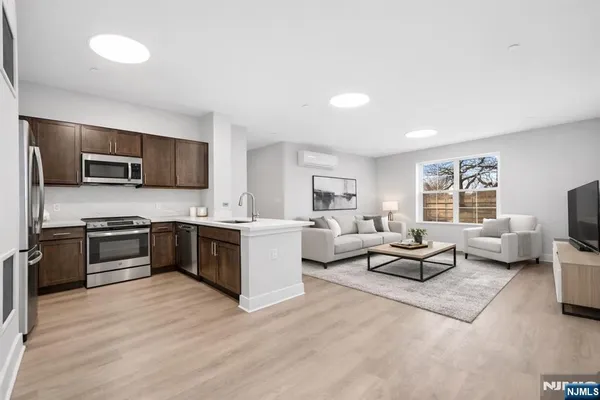 a large white open kitchen with stainless steel appliances kitchen island granite countertop a sink and a stove top oven with wooden floor