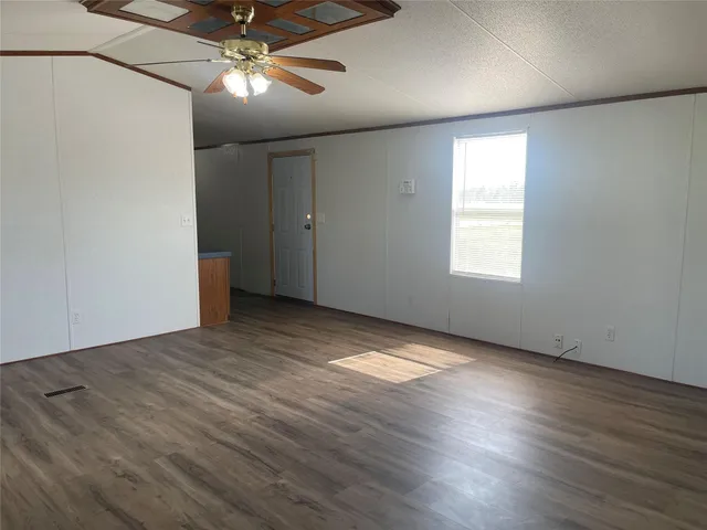 an empty room with wooden floor fan and windows