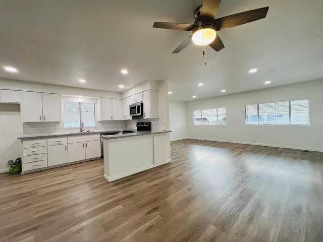 a large kitchen with granite countertop a stove top oven a sink and white cabinets with wooden floor