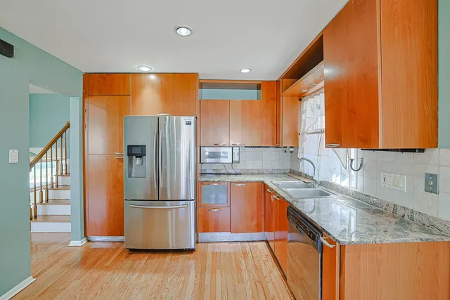 a kitchen with stainless steel appliances granite countertop a refrigerator a sink dishwasher and wooden cabinets with wooden floor