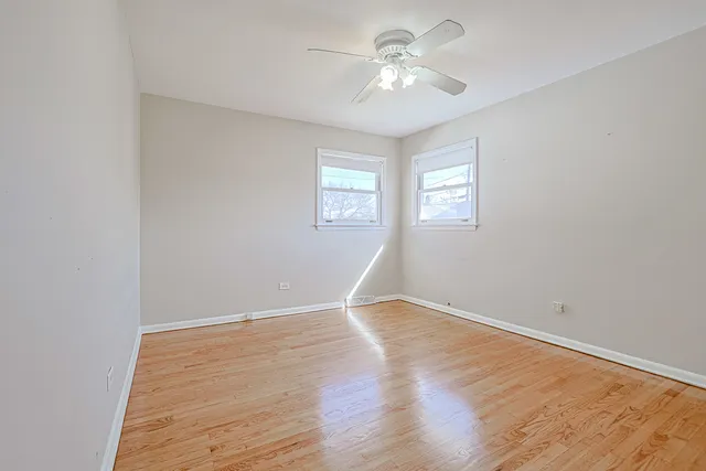 an empty room with wooden floor ceiling fan and windows