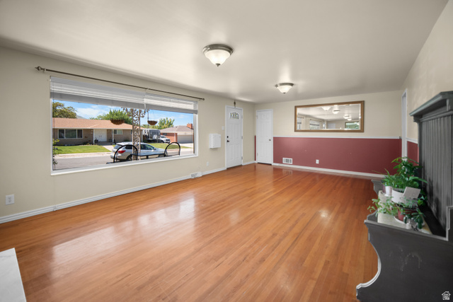 3233 Jean Street Magna, UT 84044 - Photo 4 of 33 Spacious room featuring wood-finish flooring, a large picture window with blinds, and neutral painted walls with a red wainscoting accent