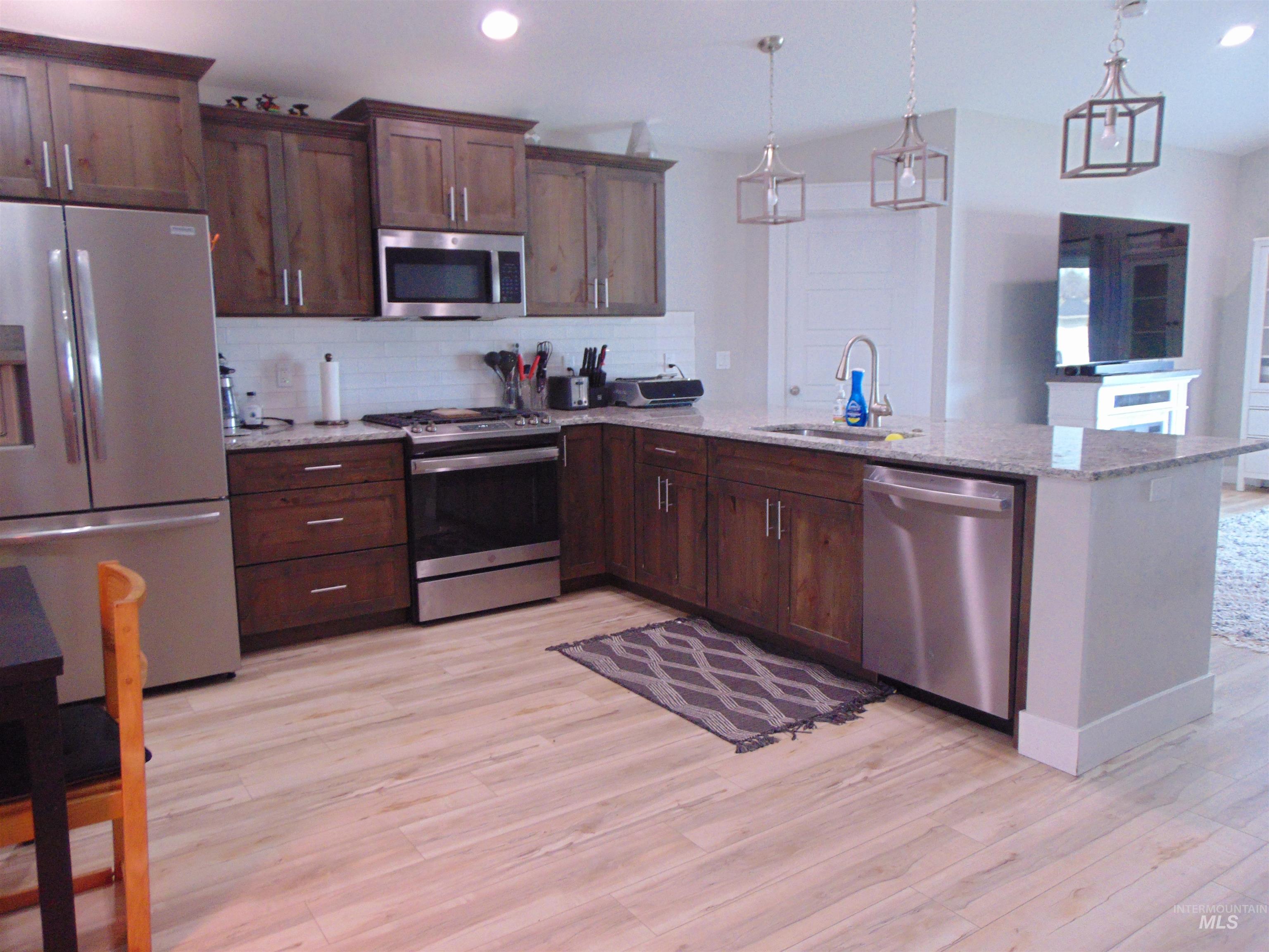 901 Campbell Street Vale, OR 97918 - Photo 4 of 22 Kitchen with stainless steel appliances, light stone countertops, decorative light fixtures, backsplash, and light wood finished floors
