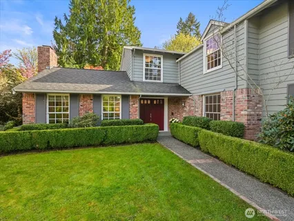 a view of a brick house with a yard plants and large tree