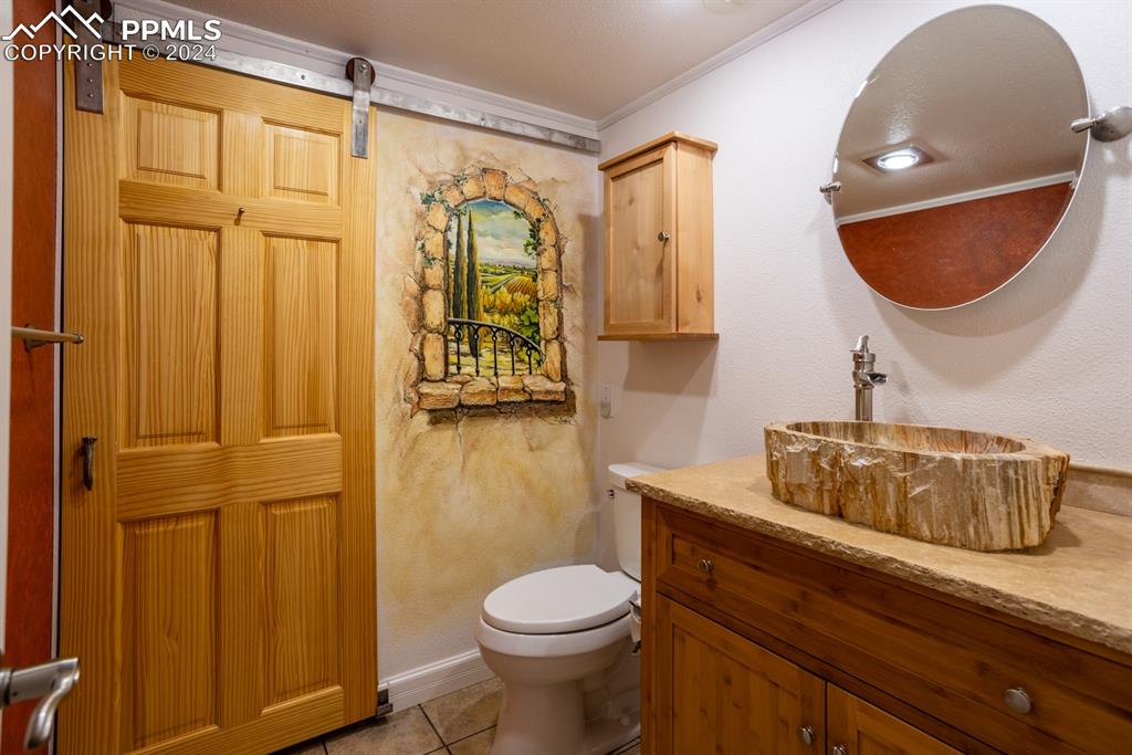 1074 Fontmore Road, Unit C Colorado Springs, CO 80904 - Photo 18 of 30 Guest bathroom featuring ornamental molding, toilet, vanity, tile patterned floors, exotic sink, painted wall mural, and barn door concealing walk-in shower