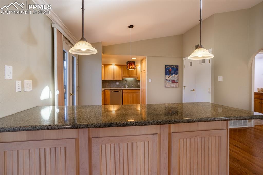1074 Fontmore Road, Unit C Colorado Springs, CO 80904 - Photo 8 of 30 A look beyond the dining area into the kitchen featuring lofted ceiling, tasteful backsplash, stainless steel dishwasher, wood-type flooring, and light brown cabinetry
