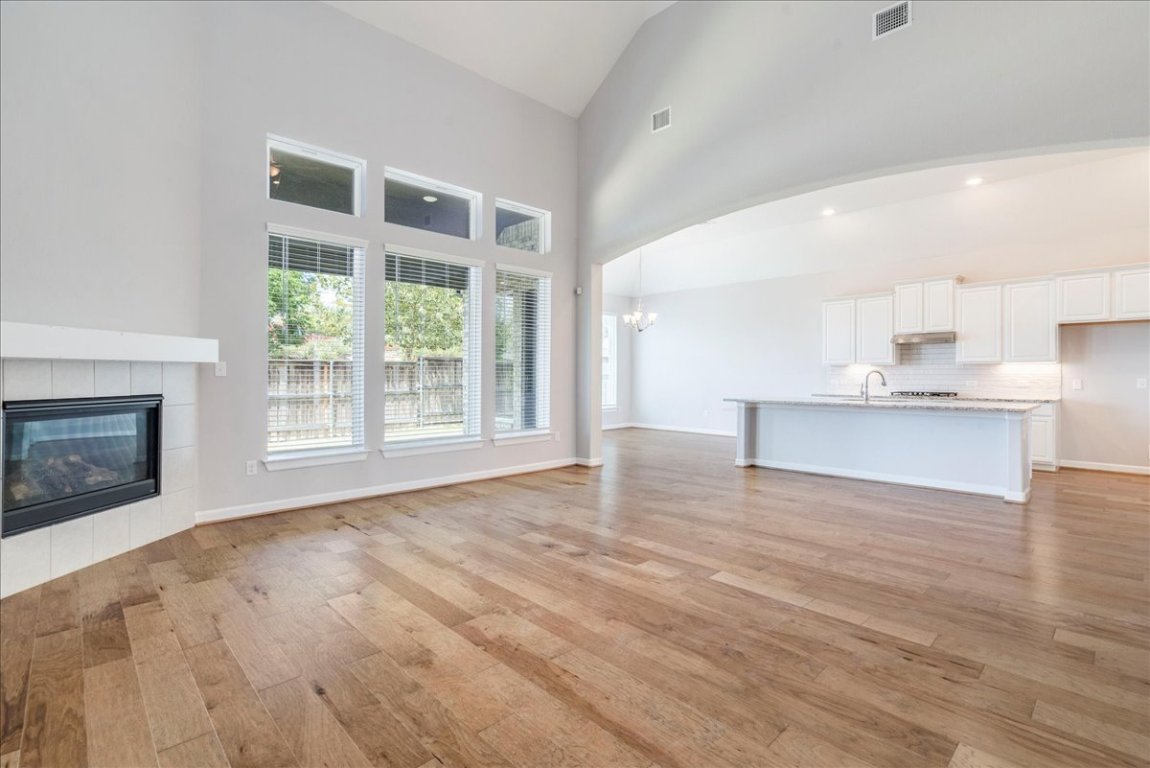 584 Baretta Loop Buda, TX 78610 - Photo 13 of 37 Unfurnished living room featuring high vaulted ceiling, a tiled fireplace, light wood flooring, and a chandelier