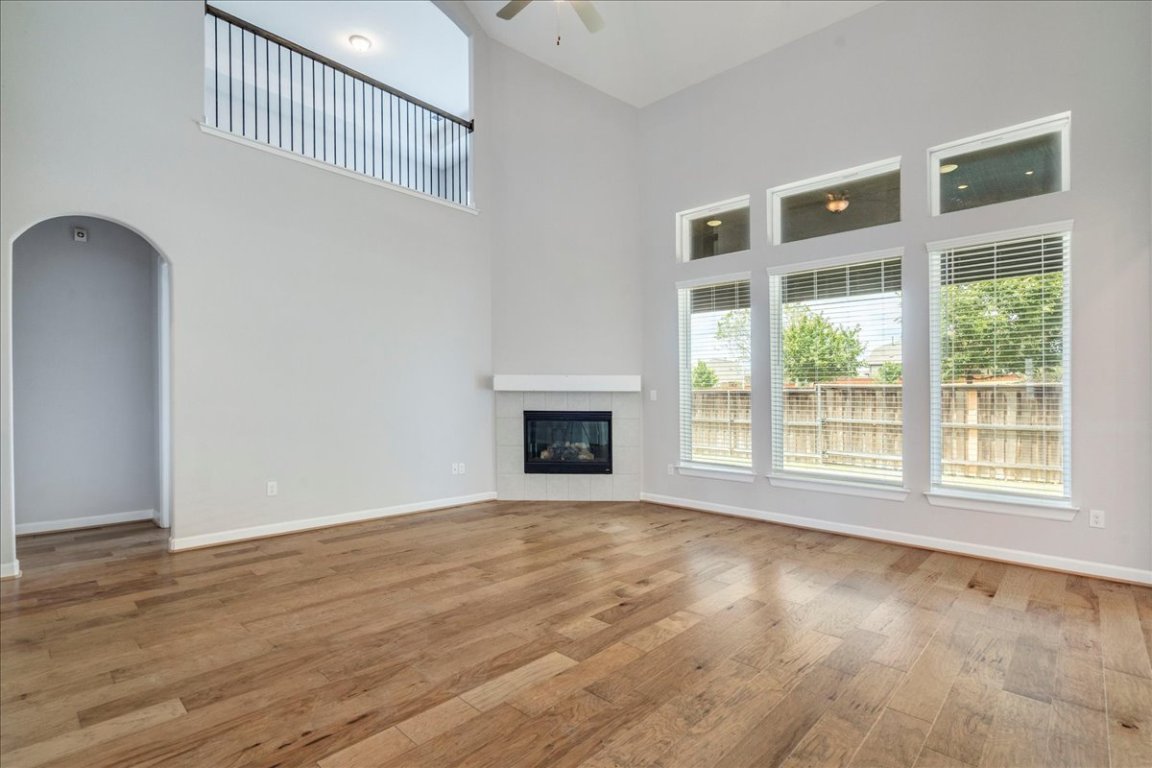 584 Baretta Loop Buda, TX 78610 - Photo 2 of 37 Unfurnished living room featuring arched walkways, a towering ceiling, light wood-type flooring, a tiled fireplace, and a ceiling fan