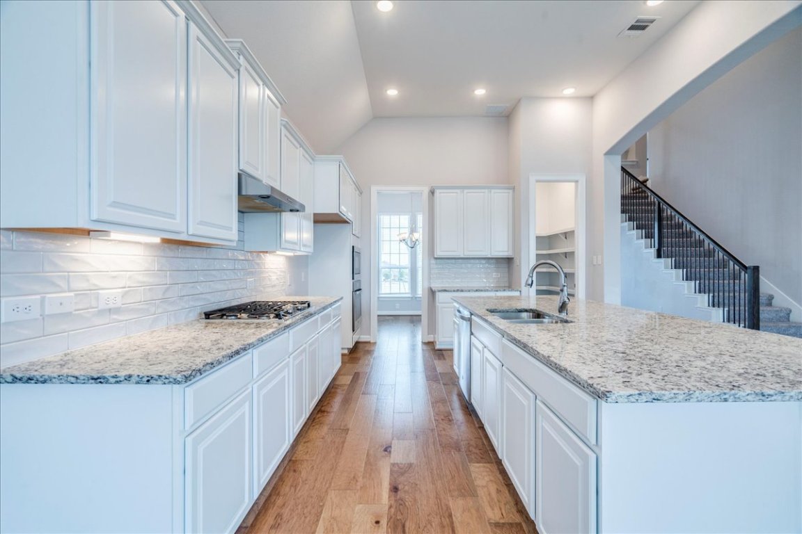 584 Baretta Loop Buda, TX 78610 - Photo 9 of 37 Kitchen with light wood finished floors, tasteful backsplash, an island with sink, light stone counters, and white cabinets