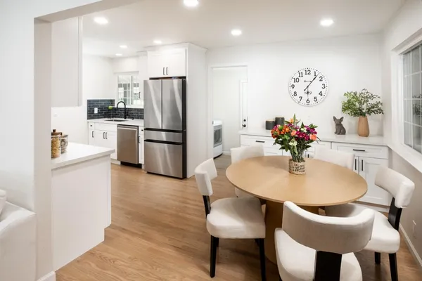 a kitchen with stainless steel appliances kitchen island granite countertop a dining table chairs and a refrigerator