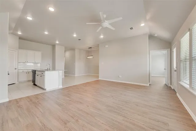 a view of an empty room with wooden floor and a kitchen