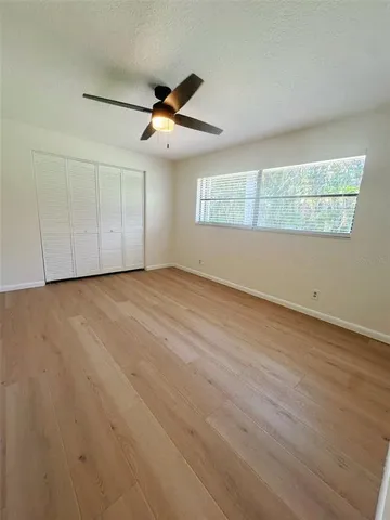 an empty room with wooden floor fan and windows