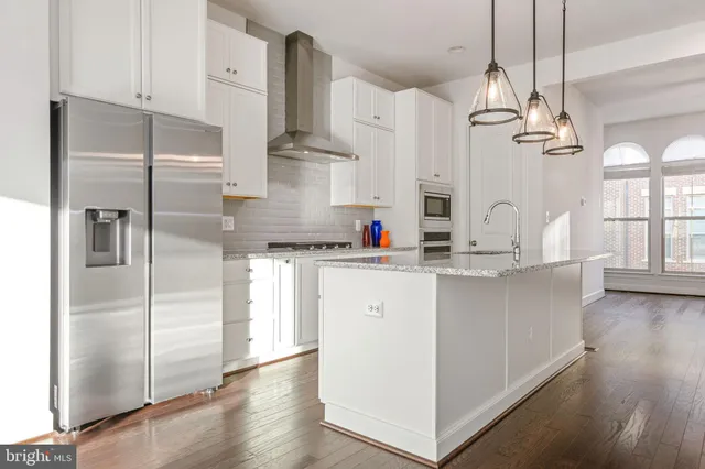 a kitchen with kitchen island granite countertop a refrigerator a sink dishwasher a oven and white cabinets with wooden floor