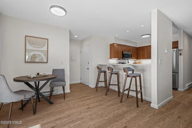 a kitchen with stainless steel appliances kitchen island granite countertop a dining table chairs and a refrigerator