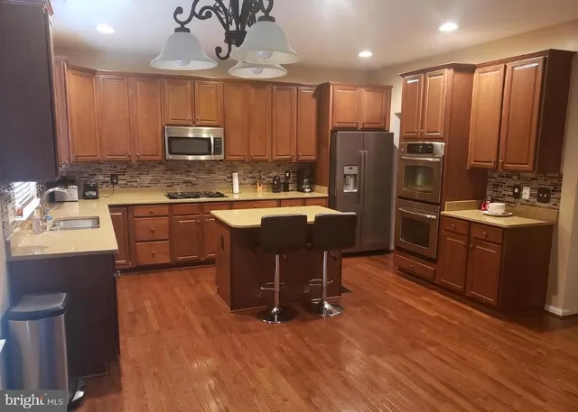 a kitchen with stainless steel appliances granite countertop a refrigerator a sink dishwasher a stove and a dining table with wooden floor