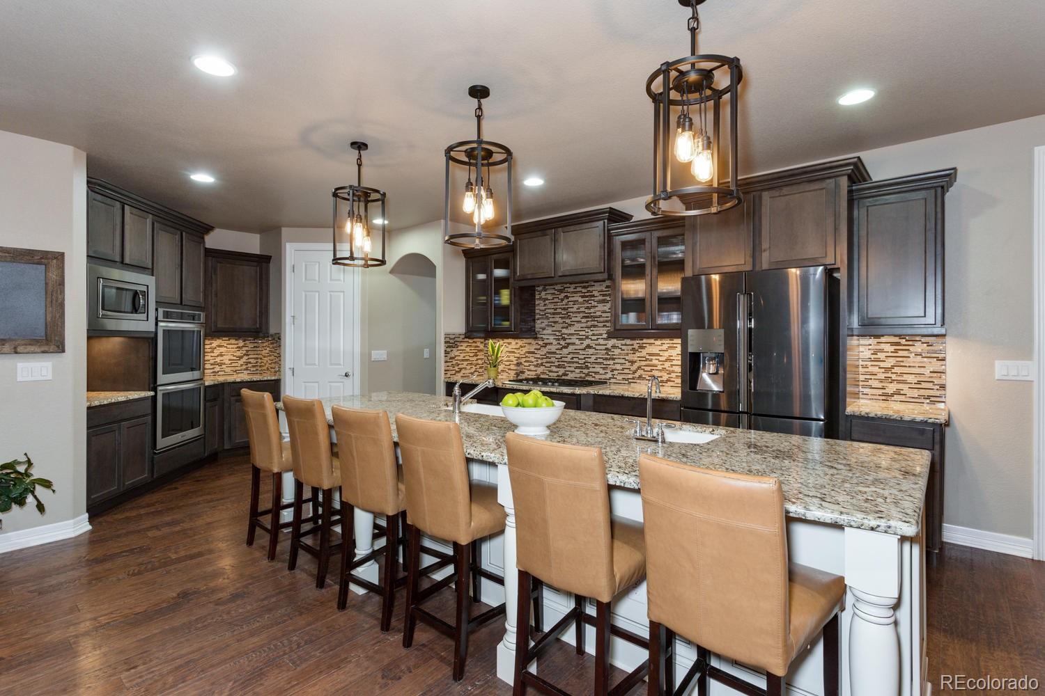 10808 Sundial Rim Road Highlands Ranch, CO 80126 - Photo 7 of 26 a kitchen with stainless steel appliances kitchen island granite countertop a dining table chairs refrigerator and microwave