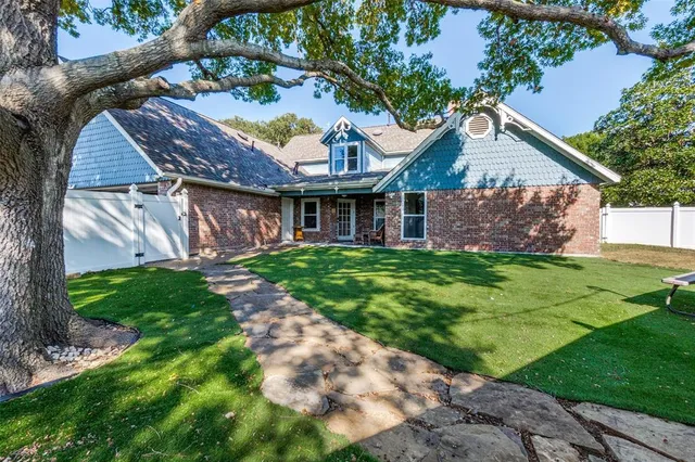 a view of a house with brick walls plants and large tree