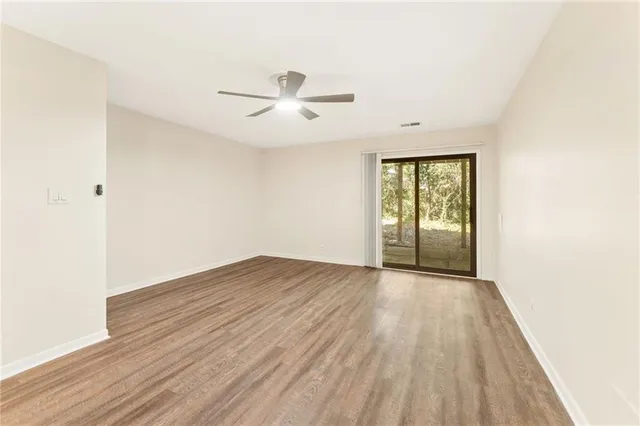 an empty room with wooden floor fan and windows