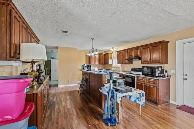 a kitchen with stainless steel appliances granite countertop a refrigerator a sink dishwasher a stove and a dining table with wooden floor