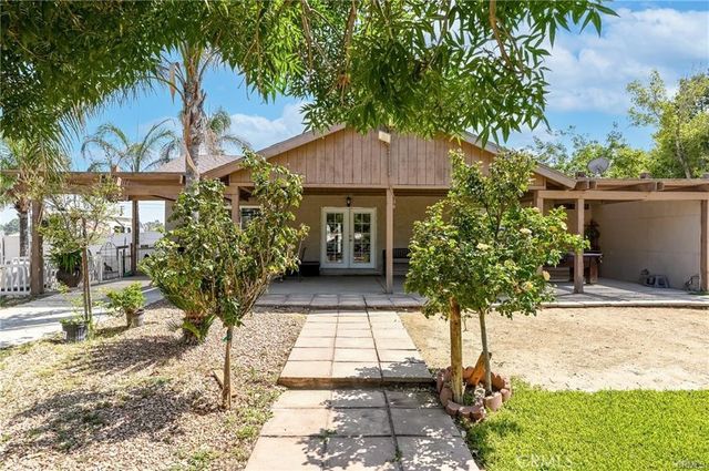 a view of a pathway of a house with potted plants and large trees