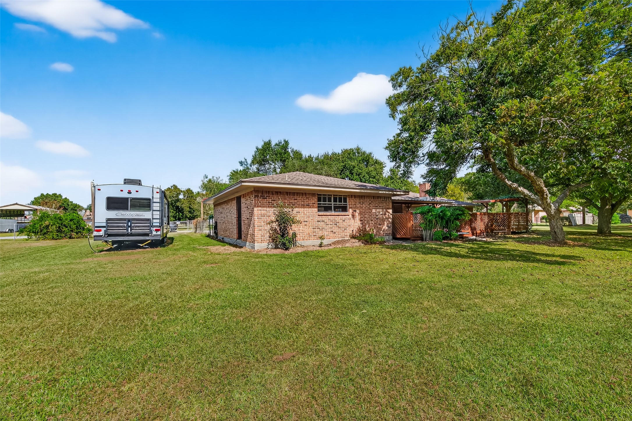 12021 7th 1/2 Street Santa Fe, TX 77510 - Photo 6 of 49 This photo shows a single-story brick house with a spacious backyard. There's a large grassy area and the property has a cozy, private feel with a covered patio area. Ideal for outdoor enthusiasts seeking ample space.