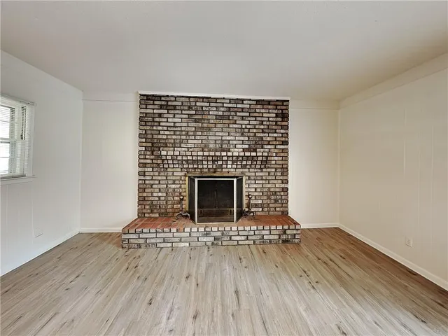 a view of an empty room with wooden floor fireplace and a window