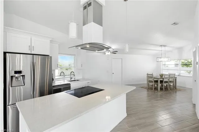 a kitchen with stainless steel appliances kitchen island granite countertop a refrigerator a stove a dining table and chairs with wooden floor