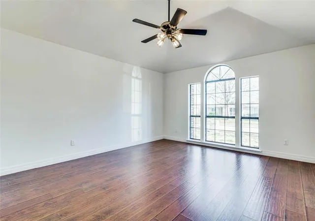 an empty room with wooden floor fan and windows